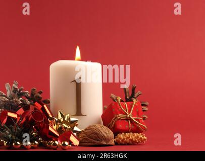 Prima candela di Avvento brucia, candela bianca con il numero uno su sfondo rosso, decorazione di Natale, spazio per il testo Foto Stock