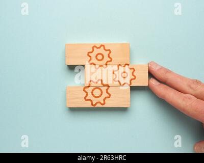 Blocchi di legno con un'icona a forma di ingranaggio su sfondo blu, una mano mette insieme i blocchi di legno Foto Stock