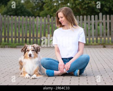 Donna con Australian Shepherd Dog al di fuori della camicia Mockup seduta sorridente Foto Stock
