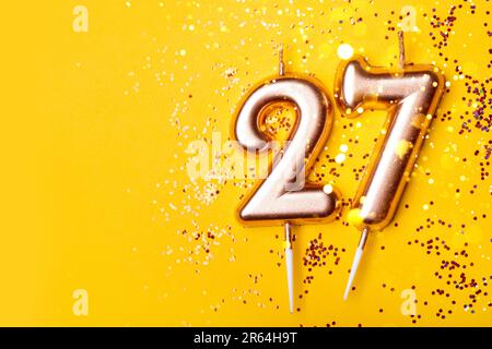 27 anni di celebrazione. Banner di saluto. Candele d'oro in forma di numero ventisette su fondo giallo con confetti. Foto Stock