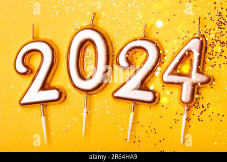 Numero 2024 da candele su un tavolo giallo con luci bokeh. Happy New Year 2024 sta arrivando il concetto. Vista dall'alto. Foto Stock
