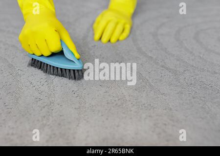 concetto di purezza e igiene - primo piano delle mani in guanti di gomma gialla pulizia tappeto grigio con spazzola, copia spazio su tappeto Foto Stock