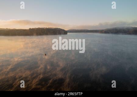 Una tranquilla scena di un lago circondato da una vegetazione lussureggiante, con nebbia che ondeggia sulla superficie Foto Stock