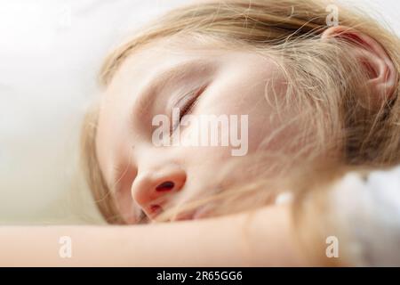 La bambina bionda calma dorme su un morbido cuscino bianco in un comodo e accogliente letto. Bambino con occhi chiusi ritratto primo piano. App sleep che tiene traccia del sonno profondo così Foto Stock