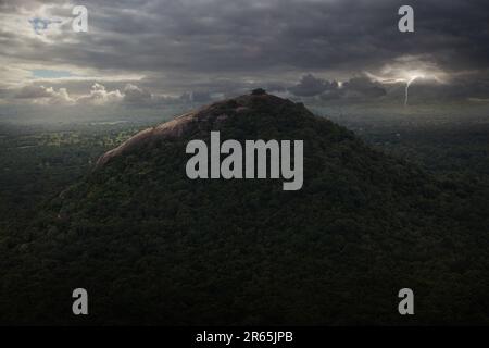 Un ampio paesaggio naturale caratterizzato da una lussureggiante cima verde di montagna, parzialmente oscurata da un velo di nuvole bianche Foto Stock