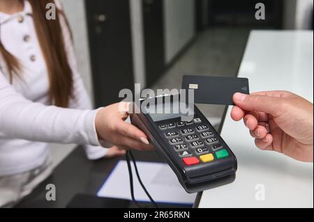 Primo piano manager al banco della reception che tiene fuori il terminale POS al cliente che paga con carta di credito. Tecnologia NFC Foto Stock