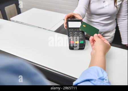 Addetta al ricevimento con lettore di carte di credito al banco della reception con carta di credito femminile. Foto Stock