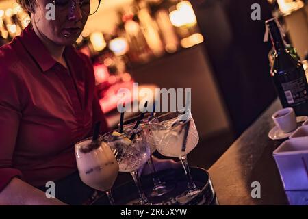 Masi, Italia 7 giugno 2023: Barista esperto che mescola e guarnisce vari cocktail dietro il bar. Foto Stock
