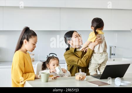 Due amici giocano con i loro figli mentre si siedono in cucina a casa Foto Stock