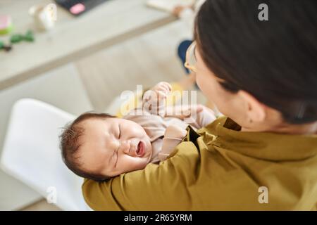 Vista posteriore della giovane mamma che tiene il suo bambino sulle braccia e lulling lui a dormire Foto Stock