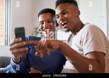 Felice giovane coppia gay maschio utilizzando smartphone a casa Foto Stock