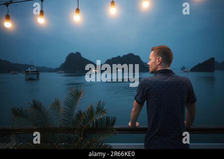 Uomo che gode di una magnifica vista notturna dalla nave da crociera tra le isole. Popolare meta turistica con formazioni carsiche in mare, ha Long Bay in vie Foto Stock