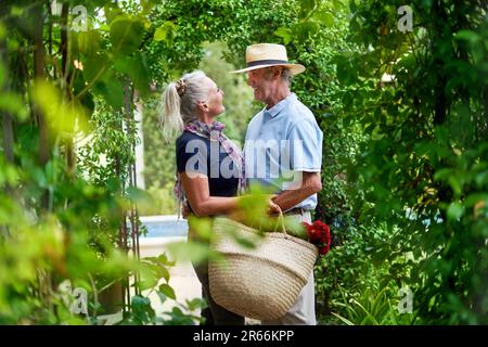 Felice coppia anziana abbracciando sotto lussureggianti graticci verdi nel giardino estivo Foto Stock