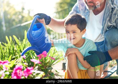 Ritratto ragazzo felice con sindrome di Down innaffiare fiori con padre Foto Stock
