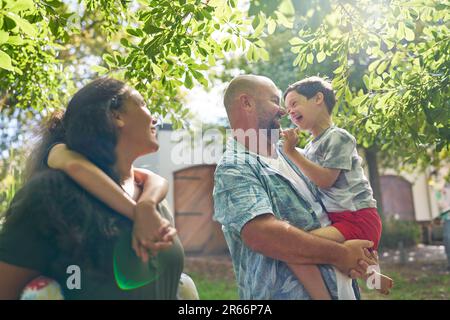 Genitori felici e figlio con sindrome di Down sotto l'albero soleggiato Foto Stock