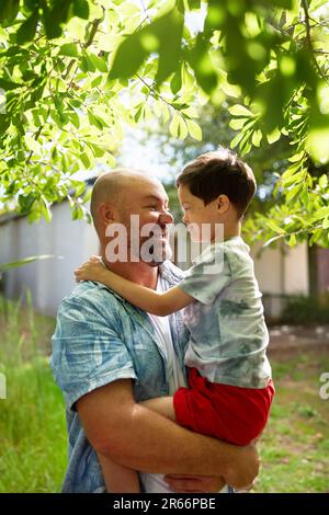 Felice padre che tiene il figlio carino con la sindrome di Down nel cortile Foto Stock