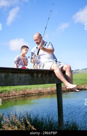 Padre che insegna figlio con Down Syndrome pesca sul molo estivo Foto Stock