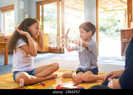 Sorella giocando gioco di clapping con fratello con sindrome di Down a casa Foto Stock