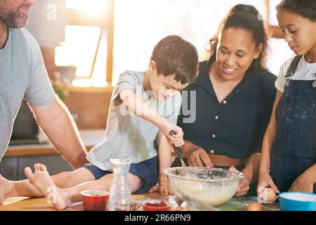 Ragazzo felice con Down sindrome di cottura con la famiglia in cucina Foto Stock