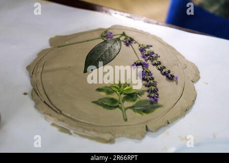Creazione di ceramica stencil con fiori e foglie di lavanda e altre piante premendo sul tavolo Foto Stock