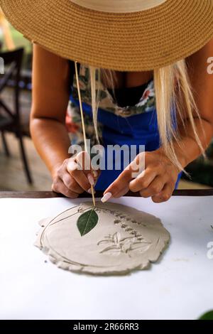 Bella giovane donna fa un'impressione di piante su uno stampo per la produzione di ceramica stencil Foto Stock