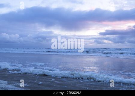 Mare con cielo nuvoloso, mare tempestoso e spiaggia sabbiosa e schiuma raccolta sulla riva Foto Stock