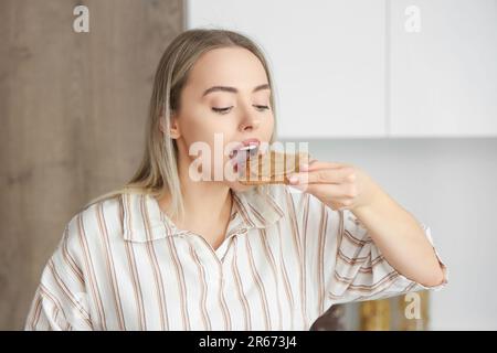 Giovane donna che mangia brindisi con burro di noce in cucina, primo piano Foto Stock