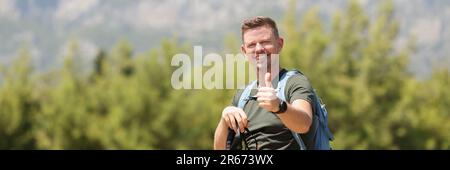 Uomo sorridente con bastoni da passeggio scandinavi e cartello con il pollice in alto Foto Stock