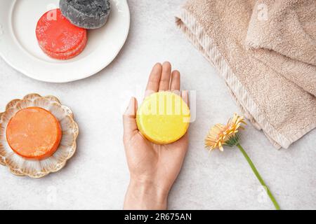 Mano femminile con shampoo massiccio fatto a mano e fiore di calendula su sfondo chiaro Foto Stock