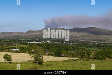 Killearn, Stirling, Scozia, Regno Unito. 7th giugno, 2023. Il servizio antincendio e di soccorso scozzese ha lanciato un avvertimento in tutta la Scozia riguardo a un rischio di incendio selvaggio "molto elevato". Nella foto: Nuvole di fumo da un fuoco selvatico che brucia sulle campsie Fells come visto sopra il villaggio di Killearn nel tardo pomeriggio. Scottish Fire and Rescue ha affermato che "a causa di un bombardamento in elicottero, consigliamo ai residenti locali di evitare l'area e di tenere chiuse le finestre e le porte". Credit: Kay Roxby/Alamy Live News Foto Stock