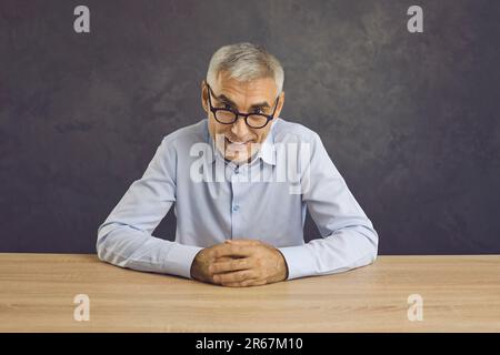 Ritratto di un uomo anziano fidato e amichevole seduto al tavolo e sorridente guardando la macchina fotografica. Foto Stock