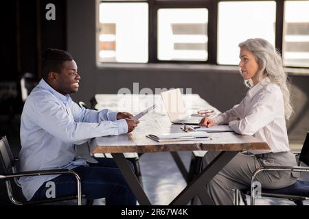 Uomo nero che parla con la signora del responsabile delle risorse umane seduta in ufficio Foto Stock