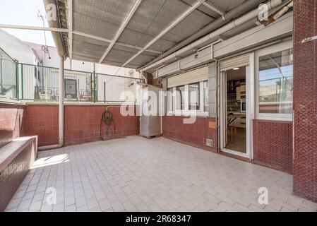 Cortile di una casa con pavimento in piastrelle bianche e piastrelle rosse alle pareti e una porta della casa in alluminio bianco e vetro Foto Stock