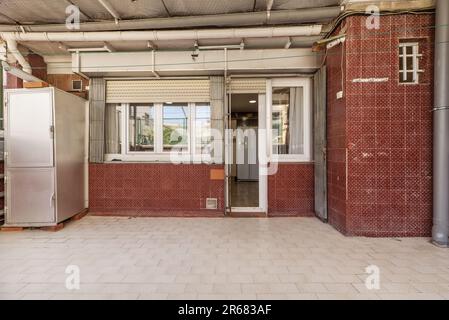 Immagine frontale di un patio di una casa con un pavimento in piastrelle bianche e piastrelle rosse alle pareti e una porta bianca in alluminio e vetro Foto Stock