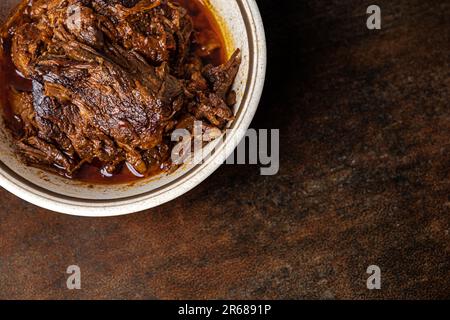 Una ciotola di birria cotta lentamente e brasata in una ciotola d'annata su fondo marrone scuro con spazio copia Foto Stock