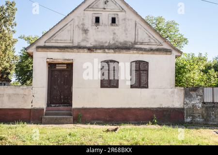 Foto di una fattoria abbandonata in Vojvodina, in Serbia, con la facciata della sua casa principale gravemente danneggiata e decadente. Foto Stock