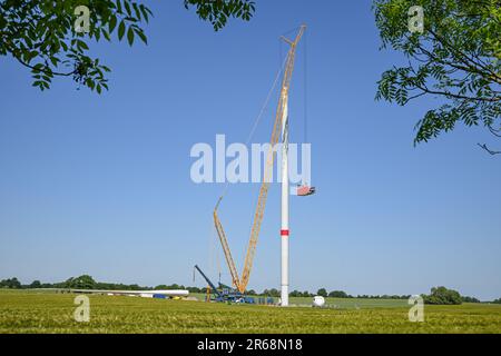 Installazione di una turbina eolica, gru alta che solleva la navicella sulla torre, mozzo del rotore, pale e generatore sdraiati sul cantiere, rinnovo Foto Stock