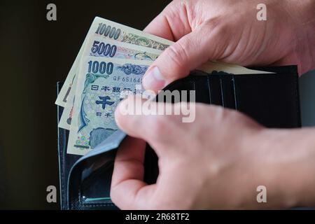 Mano che tiene un portafoglio con banconote Yen giapponesi. Foto Stock