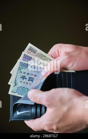 Mano che tiene un portafoglio con banconote Yen giapponesi. Foto Stock