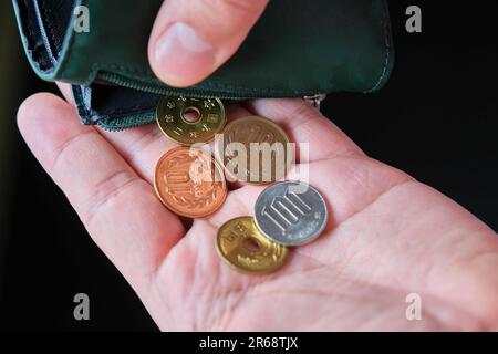 Mano che tiene un portafoglio con monete di yen. Foto Stock