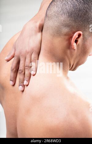 Dalla schiena, un uomo calzato solleva il braccio, avvicinandosi alla base del collo. Le tensioni muscolari, il dolore al collo o l'emicrania sono un problema? La testa è perfettamente radente Foto Stock