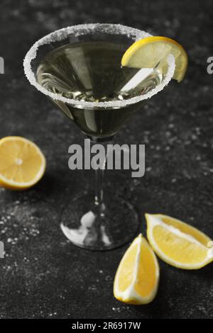 Bicchiere Martini di cocktail rinfrescante decorato con fettina di limone e zucchero sul tavolo nero testurizzato Foto Stock