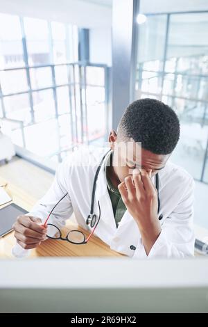 Come dirò al mio paziente? un bel giovane medico seduto da solo nel suo ufficio in clinica e utilizzando il suo computer. Foto Stock