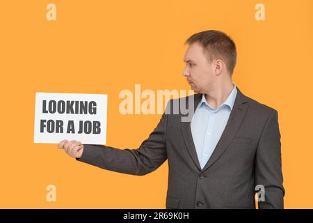 Disoccupato uomo in attesa di segno con frase cercando Un lavoro su sfondo arancione Foto Stock