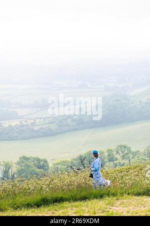 Brighton UK 8th Giugno 2023 - Un camminatore guarda il sole iniziare a bruciare attraverso la nebbia di mattina presto lungo la South Downs Way a Ditchling Beacon vicino a Brighton come il tempo caldo è previsto per i prossimi giorni in tutta la Gran Bretagna : Credit Simon Dack / Alamy Live News Foto Stock