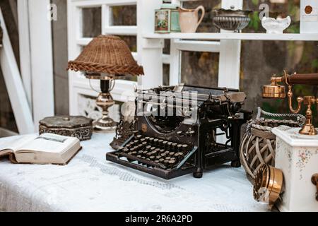 Macchina da scrivere vintage vecchio stile sulla scrivania accanto alla finestra con lampada, libri e telefono retrò in bianco chiaro scabby elegante Provenza francese d'epoca Foto Stock