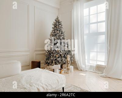 Decorazioni studio con elegante decorato albero di Natale con regali, giocattoli, nutcracker accanto a grandi finestre in bianco spazioso soggiorno con Foto Stock