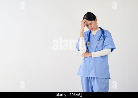 Una giovane donna asiatica stressata e affaticata medico o operatrice medica in scrub che soffrono di mal di testa o emicranie. isolato su sfondo bianco Foto Stock