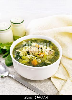 Ministra maritata con polpette, spinaci, carote, sedano e pasta fine in una ciotola, tovagliolo e cucchiaio su fondo di un tavolo di pietra Foto Stock