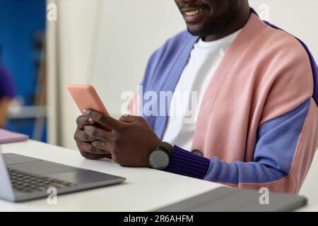 Primo piano di un uomo nero sorridente che tiene lo smartphone sul posto di lavoro in un ufficio colorato, in uno spazio per fotocopiare Foto Stock